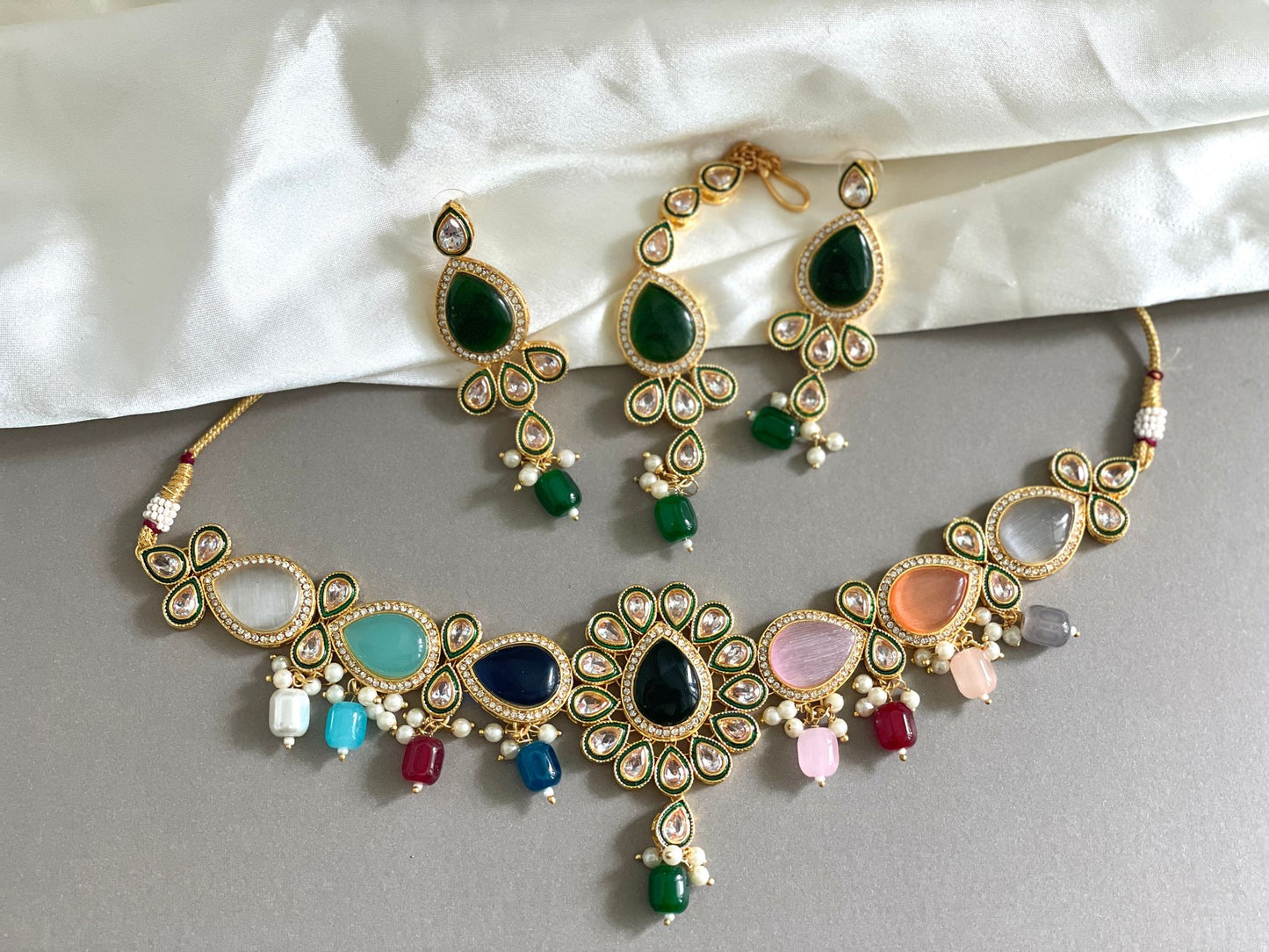 One necklace and two green earrings placed on a white sheet
